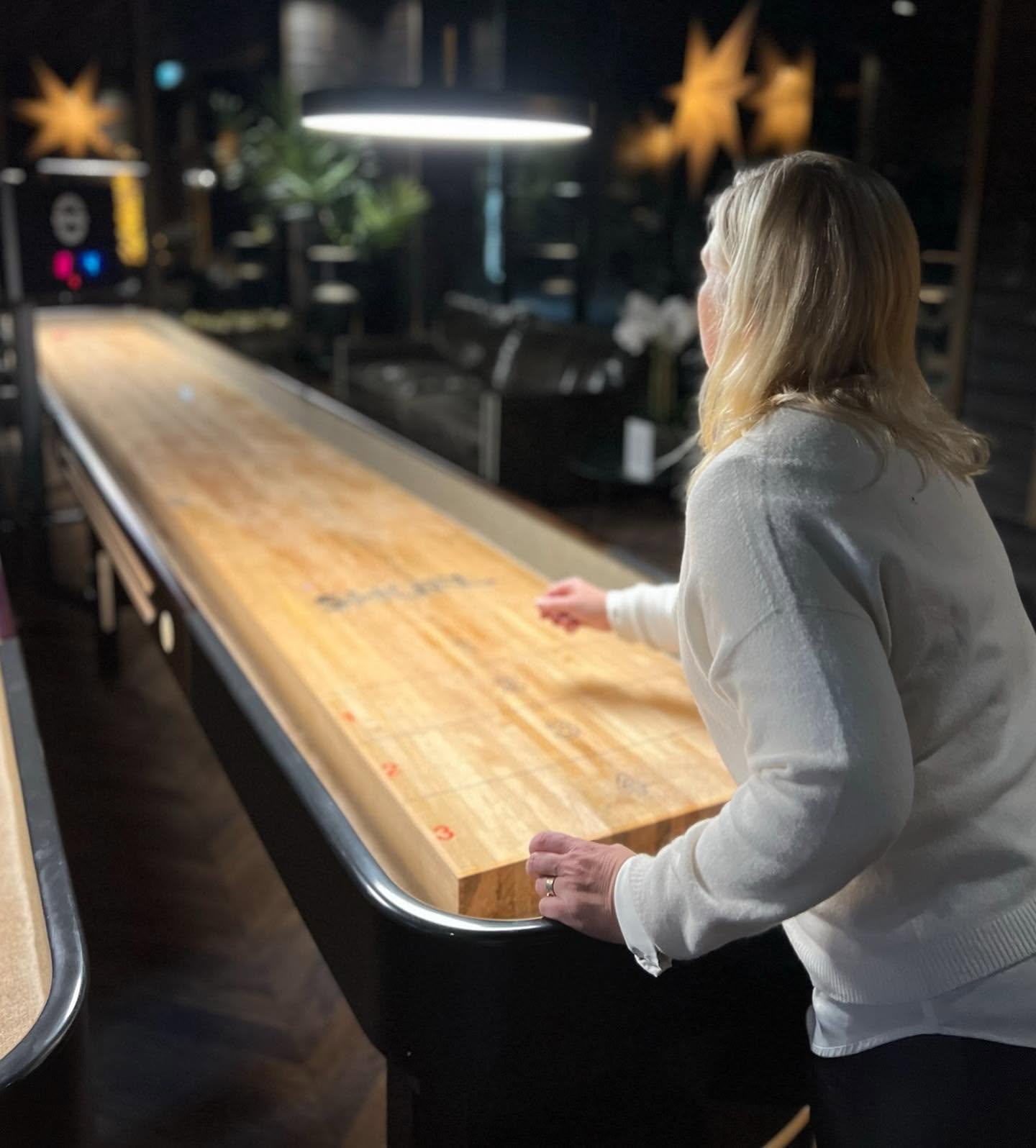 Person spelar shuffleboard på ett långt träbord inomhus