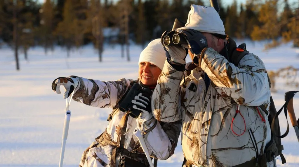 Två jägare i vinterkamouflage spanar med kikare i snölandskap